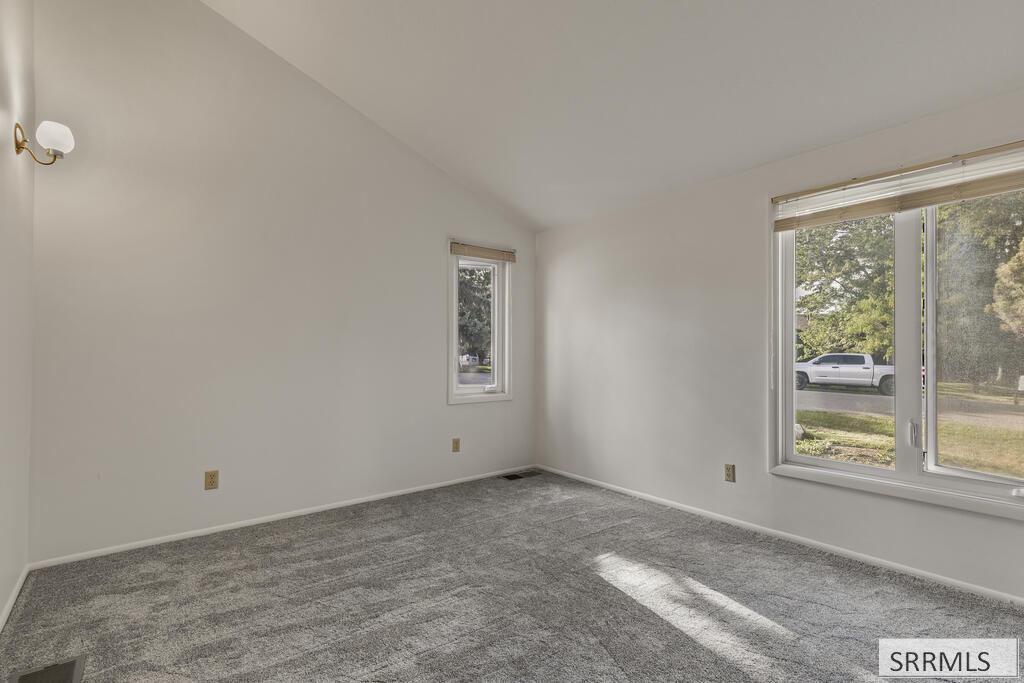 Vacant carpeted room with large windows and sunlight across the floor.