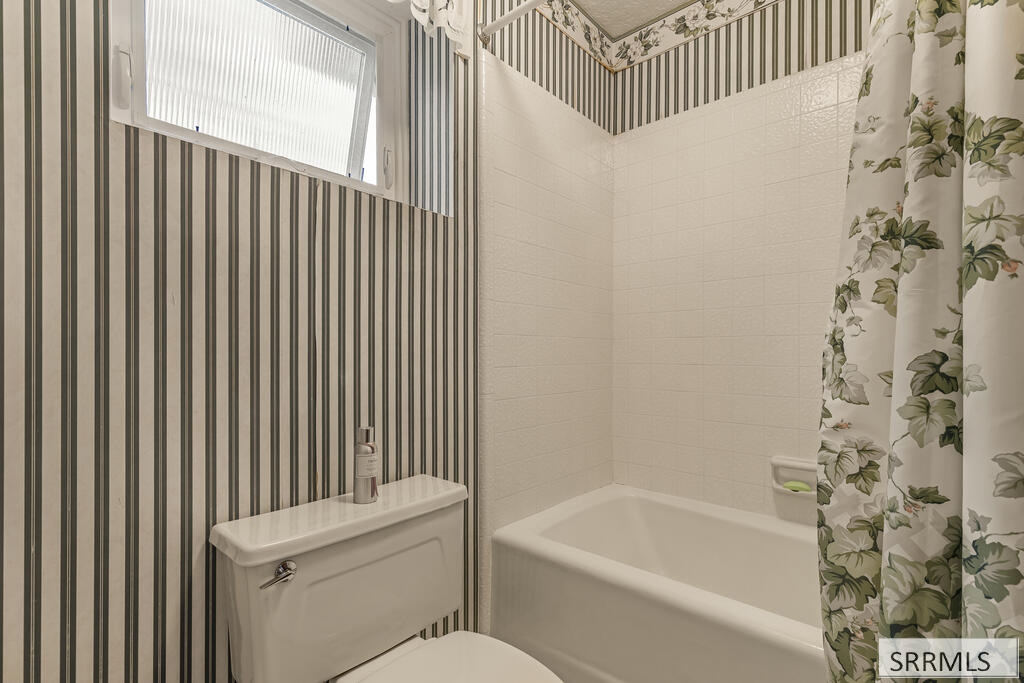 Bathroom with a white bathtub, striped wallpaper, and a floral shower curtain.