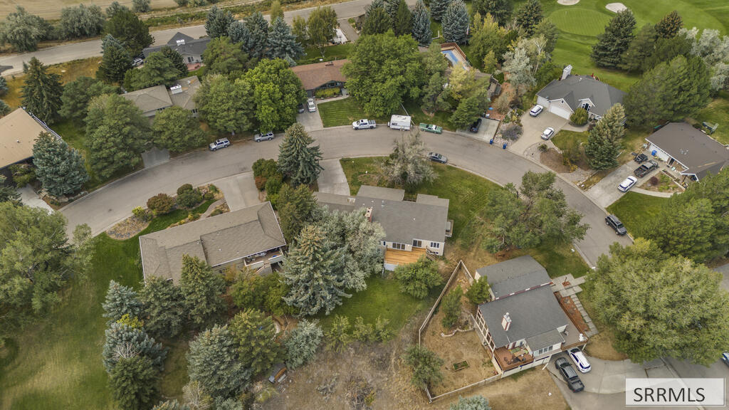 Aerial view of a home with a wooden deck on a tree-lined curved street near a golf course.