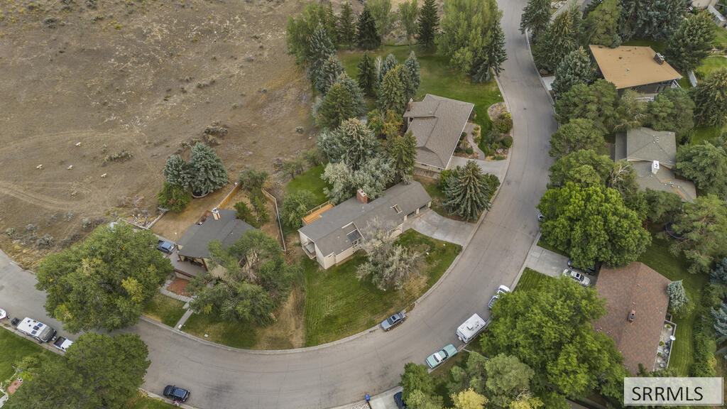 Aerial view of a single-story home on a curved street beside an open field.