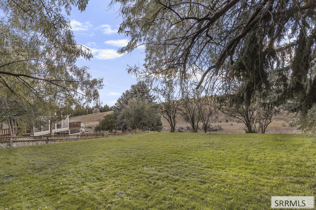 Backyard lawn beneath mature trees, with a fenced deck and rolling hills beyond.