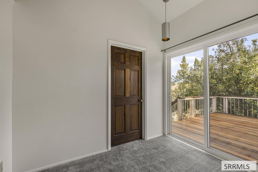 Empty carpeted room with a sliding glass door overlooking a wood deck and trees.