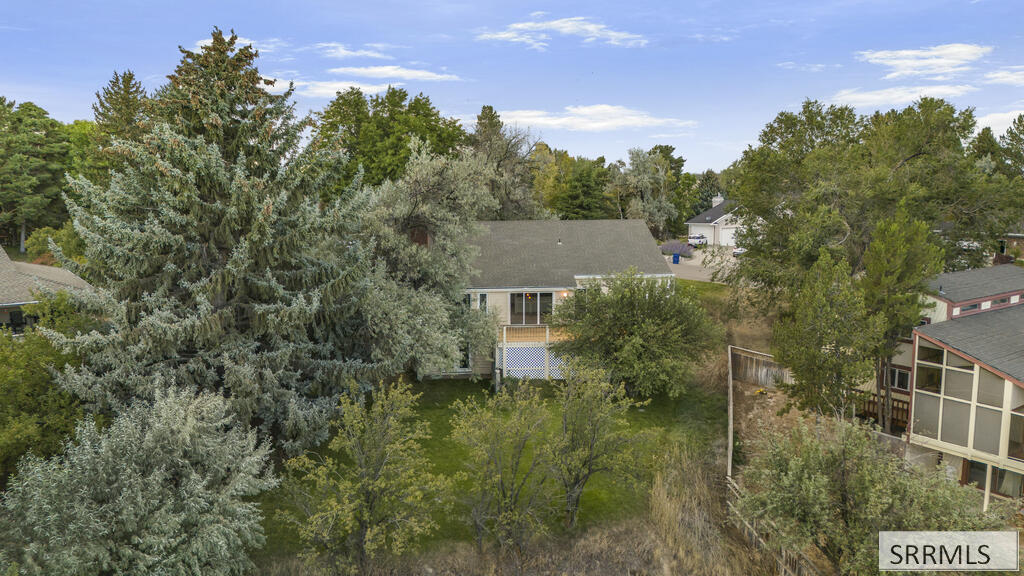Aerial view of a single-story home’s tree-shaded backyard and nearby homes.