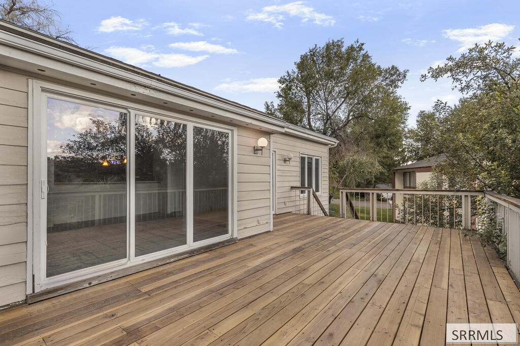 Spacious wooden deck beside sliding glass doors, with railings and mature trees.