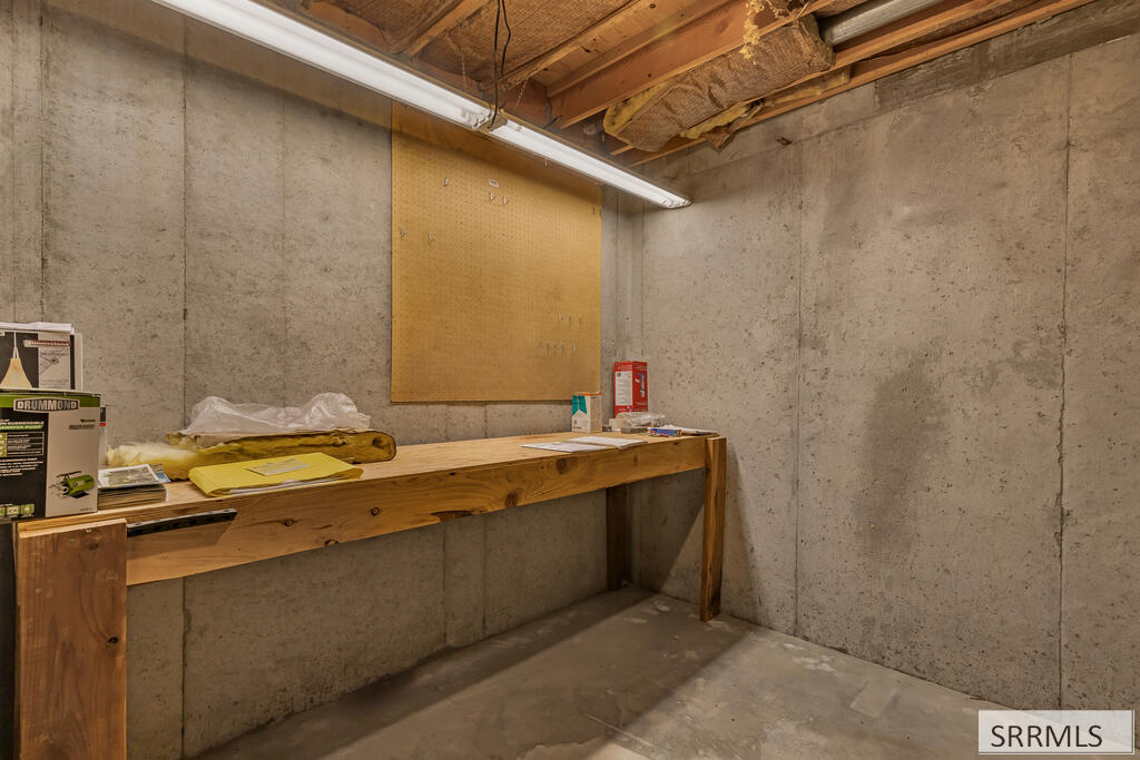Concrete basement workshop with a long wooden workbench, pegboard, and exposed ceiling joists.
