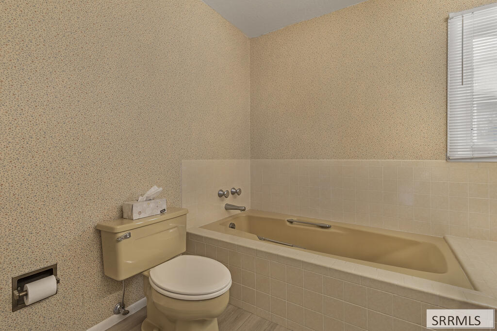 Bathroom with a beige bathtub and matching toilet beside a window with blinds.