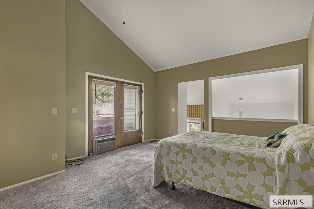 Bedroom with vaulted ceiling, patterned bedspread, and a wood-framed glass door.