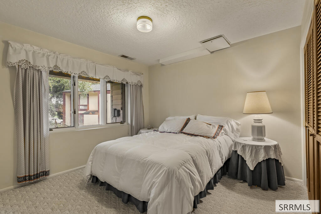Bedroom with a white bed, curtained window, and bedside table with a lamp.