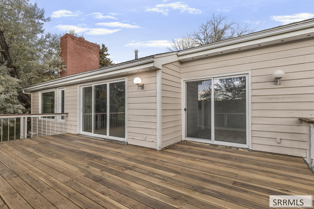 Wooden deck beside a beige-sided home, with sliding glass doors and a red brick chimney.