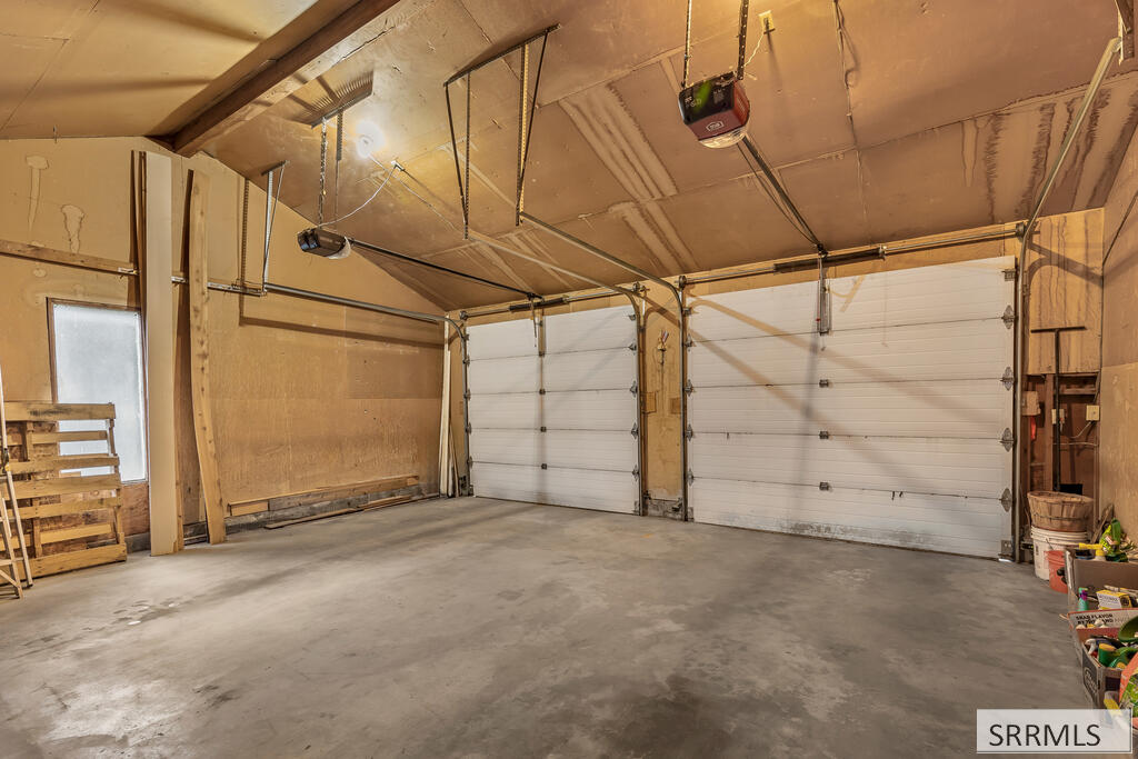 Large garage with two white overhead doors, exposed ceiling framing, and a broad concrete floor.