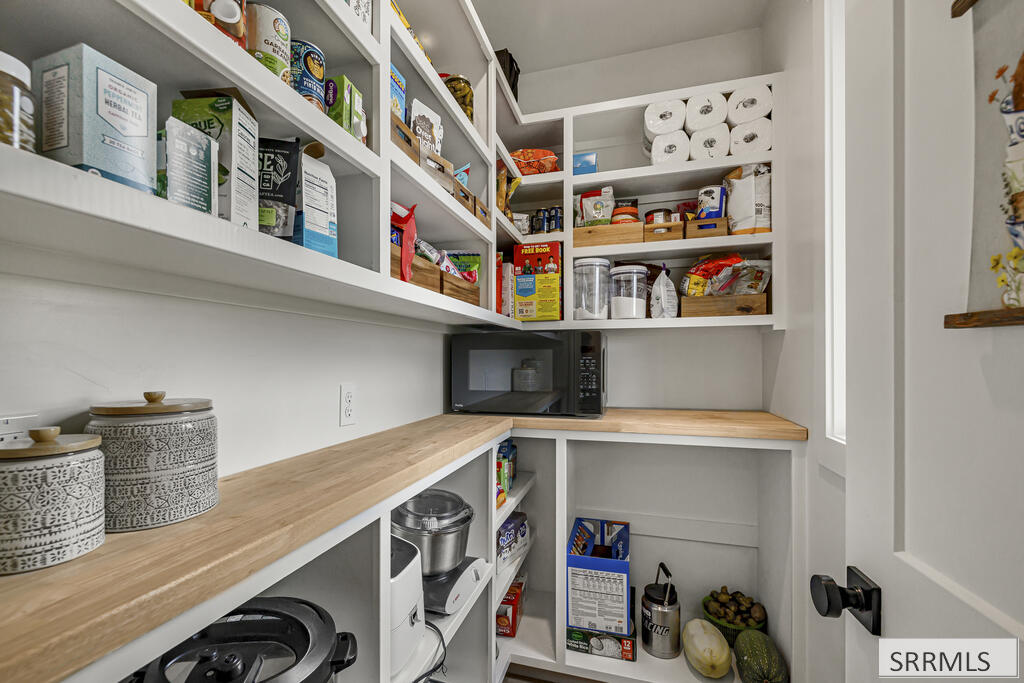 Walk-in pantry with stocked white shelves, light wood counters, and a microwave.