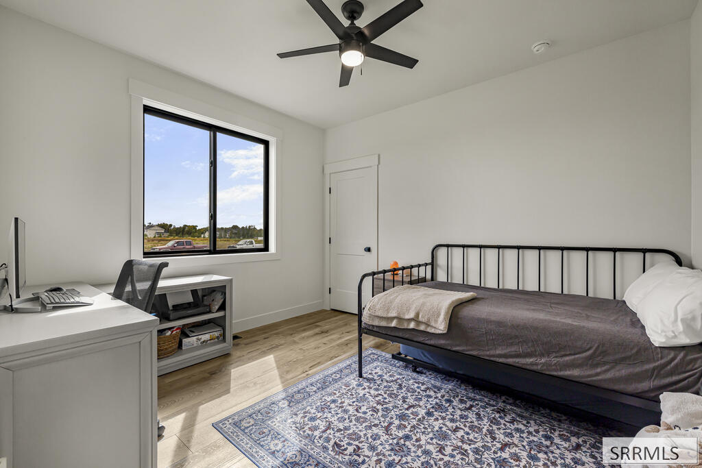 Bedroom with a black metal bed, patterned rug, desk, and large street-facing window.