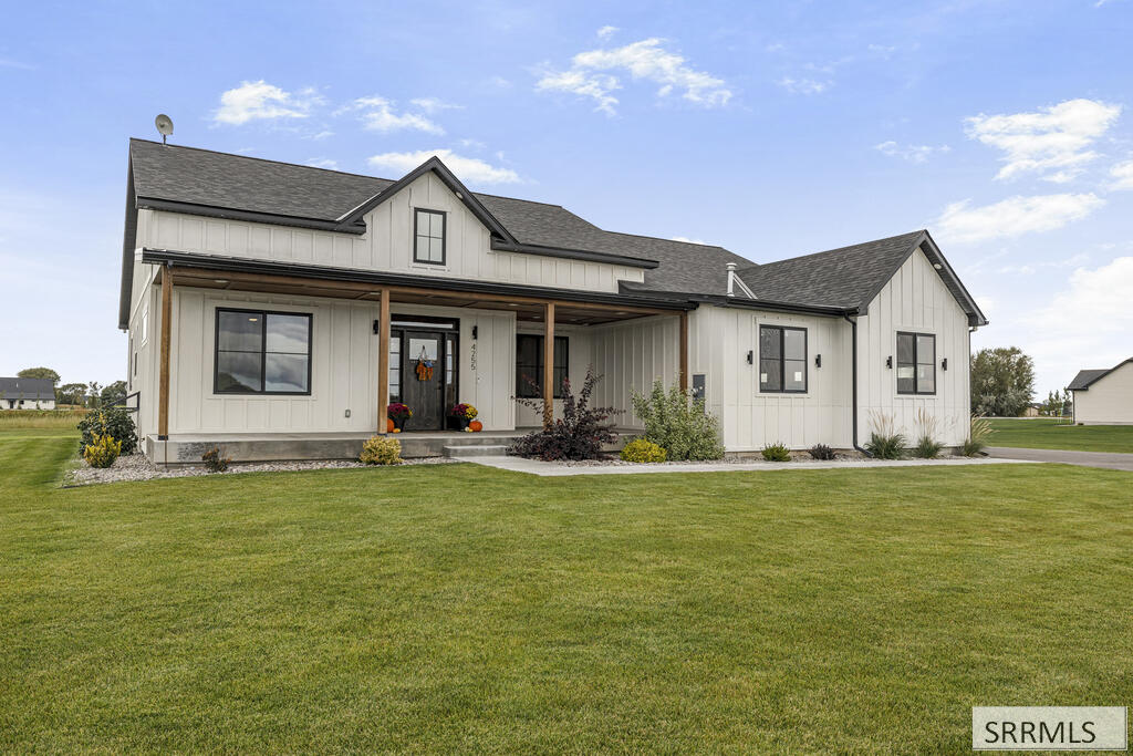 Light-colored home with a covered porch, dark gabled roof, and broad green lawn.