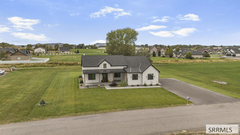 White single-story house with a dark roof, broad lawn, and long driveway, viewed from above.