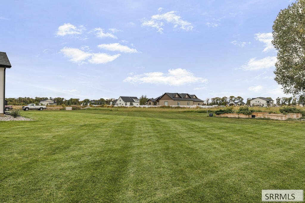 Spacious green lawn with neighboring homes and raised garden beds along the far edge.