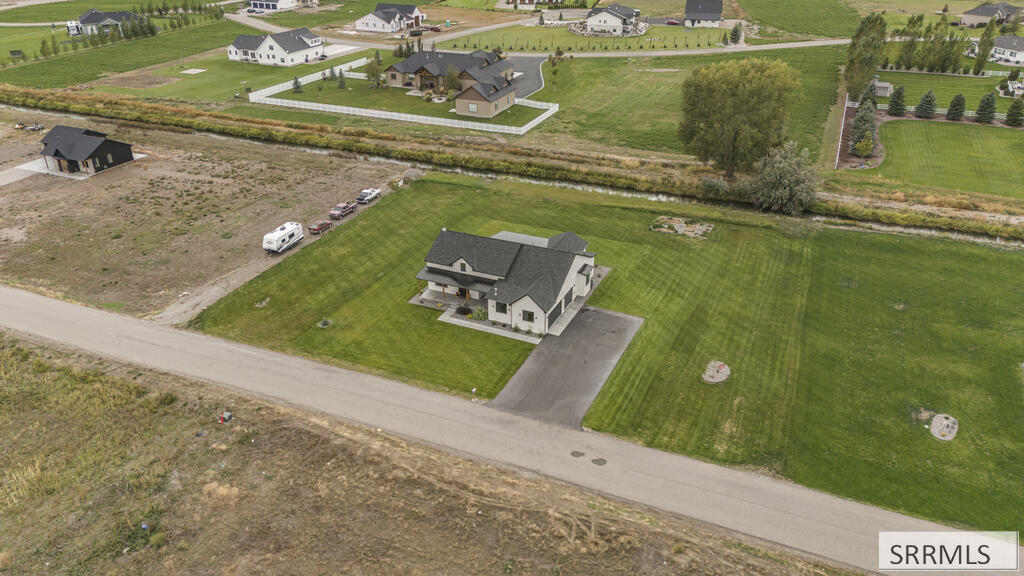 Aerial view of a white house with a dark roof, broad lawn, and long driveway beside a rural road.