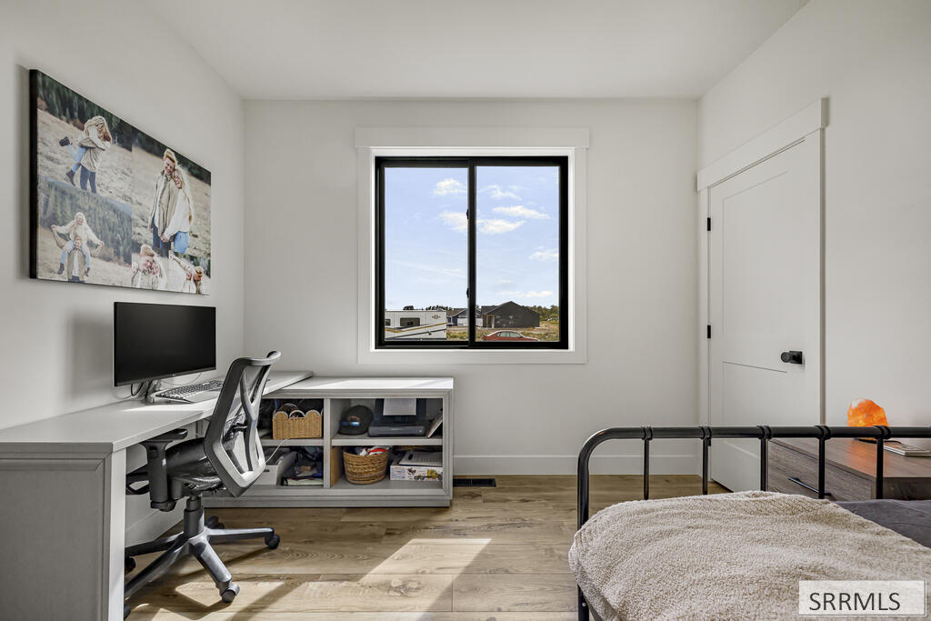 Bedroom with a black metal bed, white desk, and window overlooking neighboring homes.