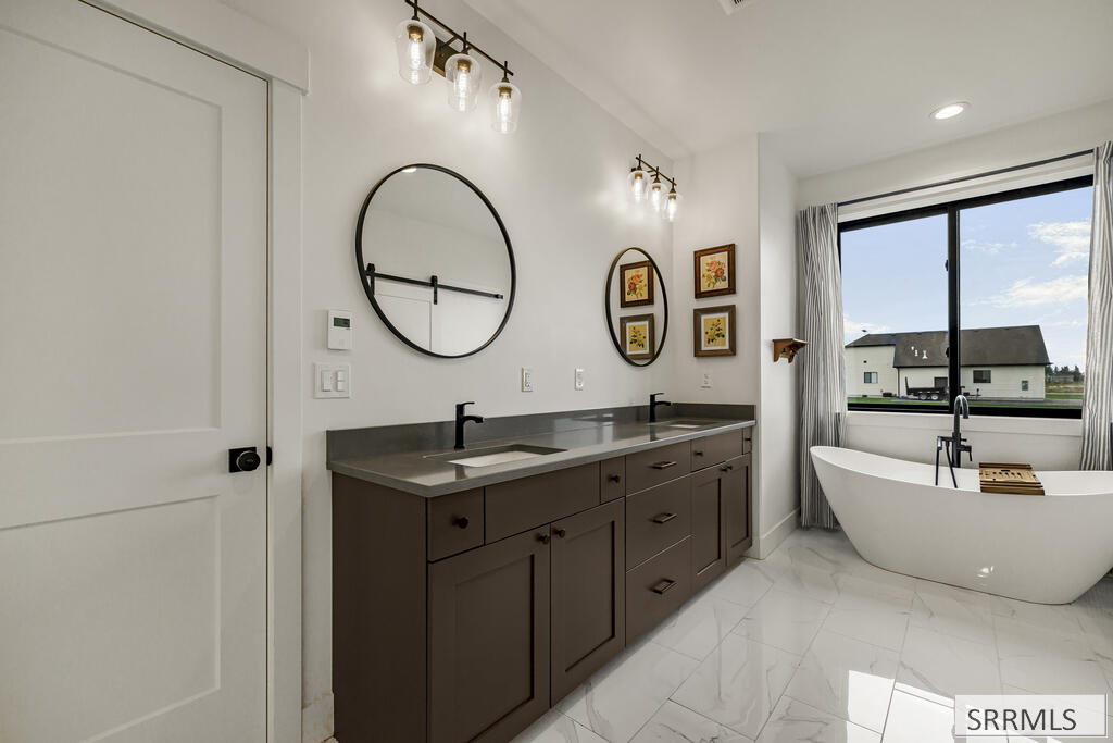 Bathroom with a dark double vanity and freestanding tub beside a large window.