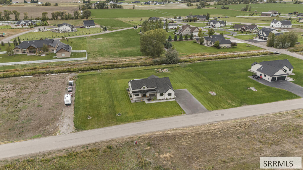 Aerial view of a house with a broad lawn and long driveway in a neighborhood beside open fields.