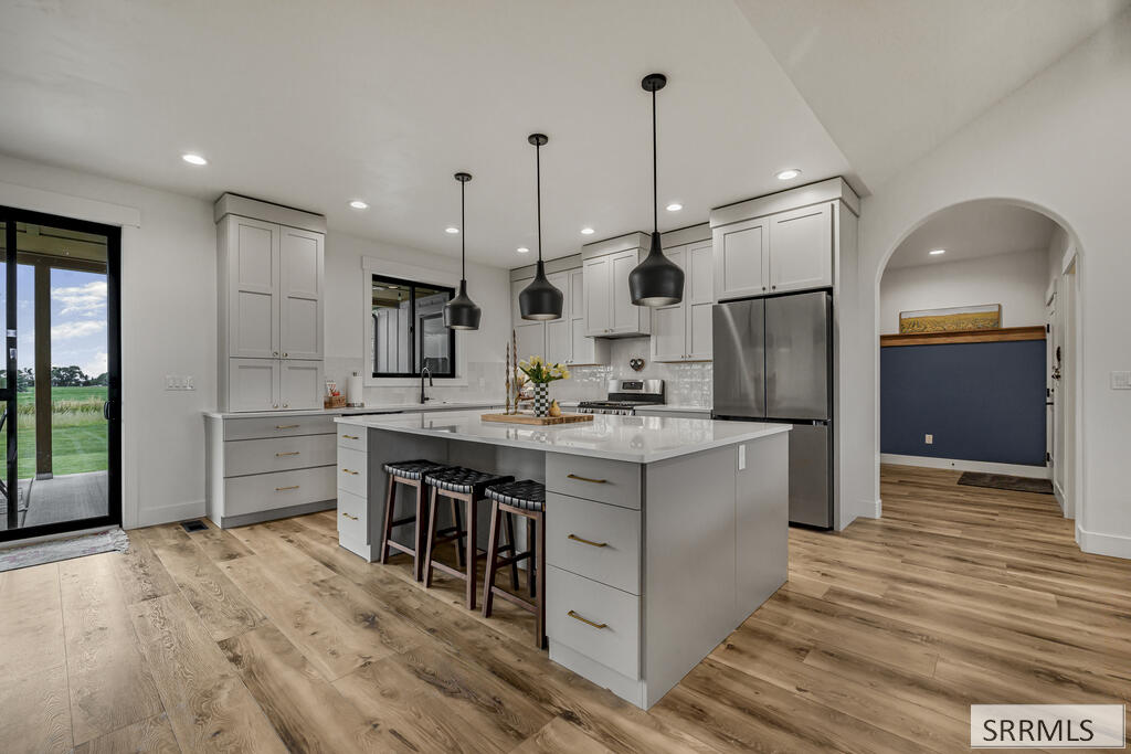 Kitchen with a large island, white shaker cabinets, stainless steel appliances, and black pendant lights.
