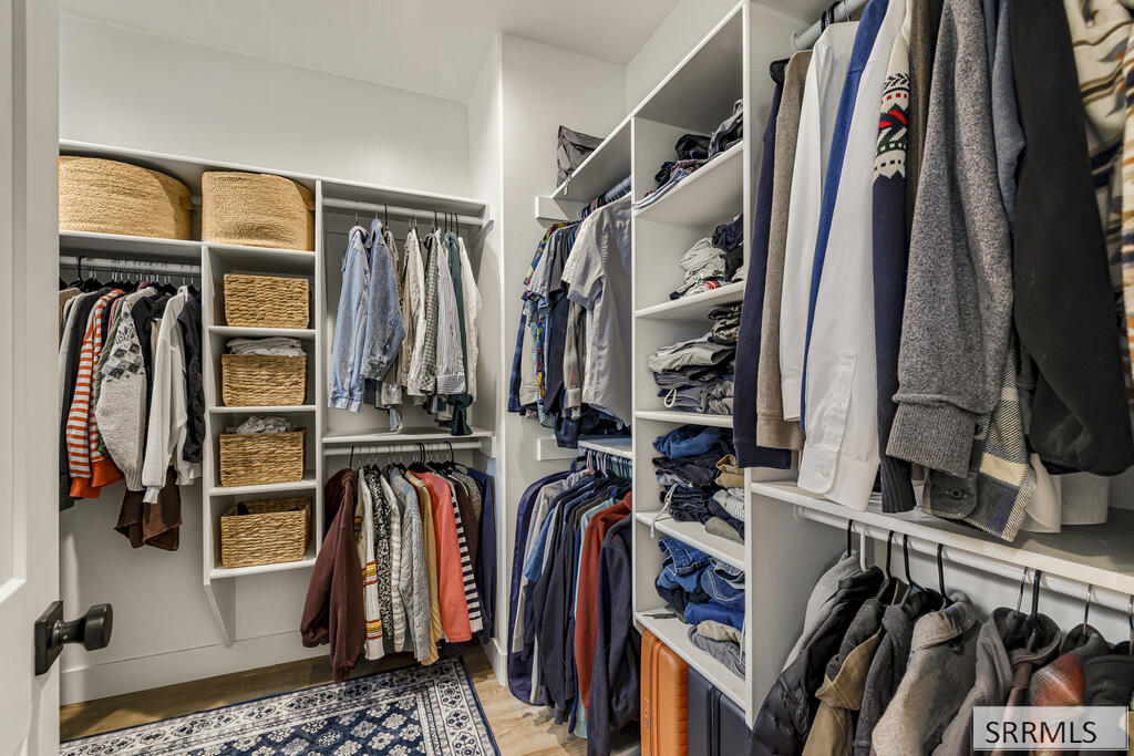 Walk-in closet with built-in shelving, hanging clothes, woven baskets, and a patterned rug.