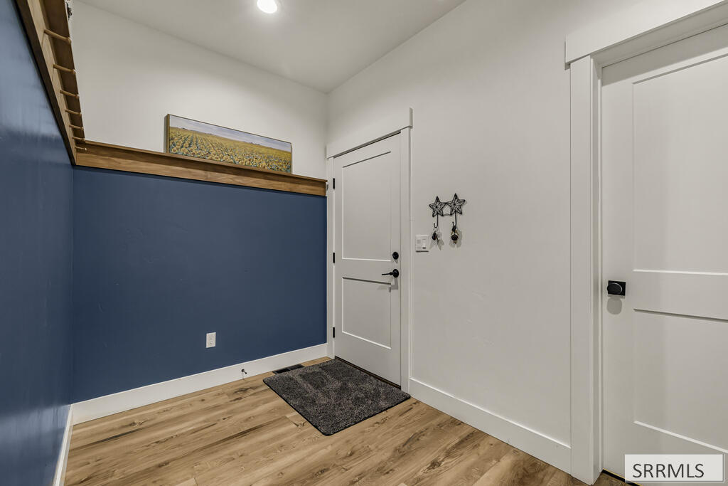 Entryway with a dark blue accent wall, wooden shelf, wood-look flooring, and two white doors.