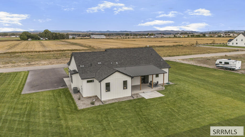 Single-story home with a covered patio and broad lawn surrounded by open fields.
