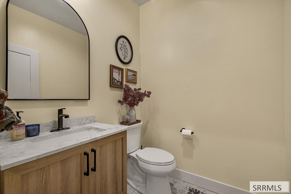 Bathroom with wood vanity, marble-look counter, black faucet, and arched mirror.