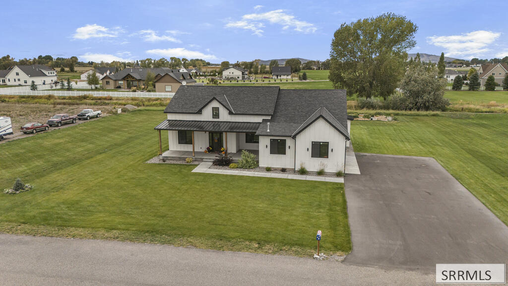 Aerial view of a white home with dark gabled roofs, a covered porch, broad lawn, and long driveway.