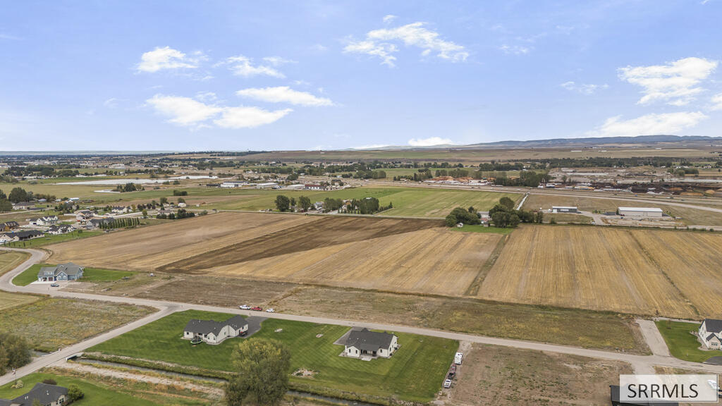Aerial view of harvested fields and scattered homes beneath a partly cloudy sky.