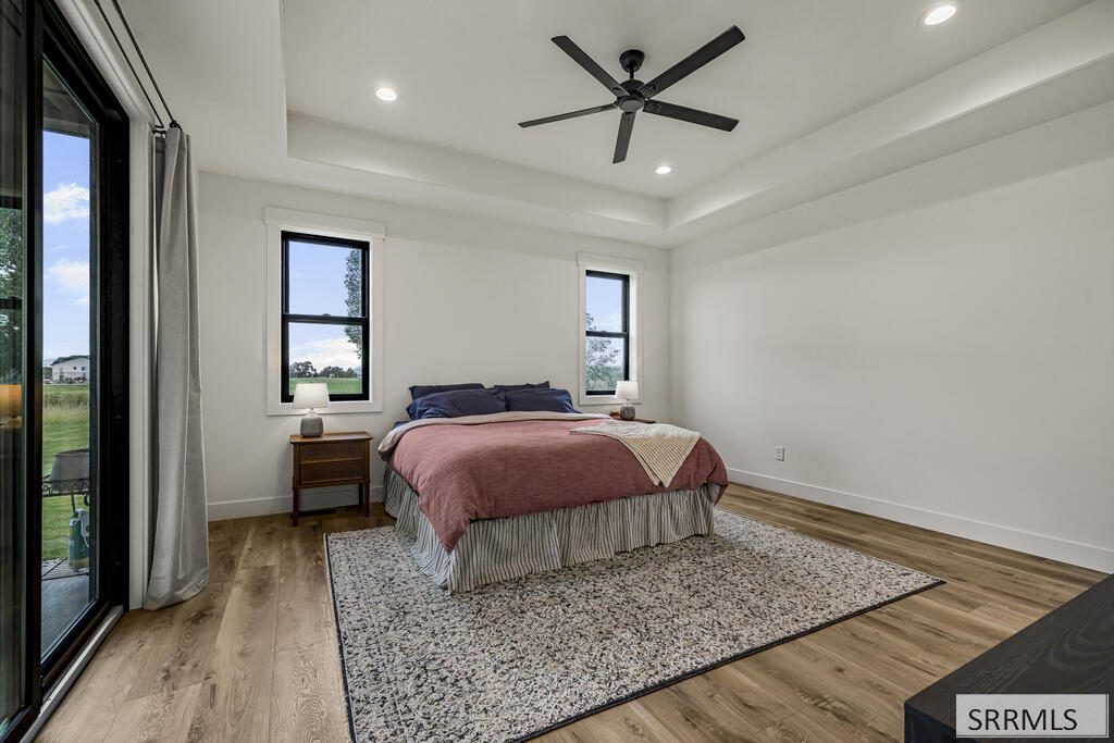 Furnished bedroom with rose bedding, a tray ceiling, and sliding glass doors overlooking a grassy yard.