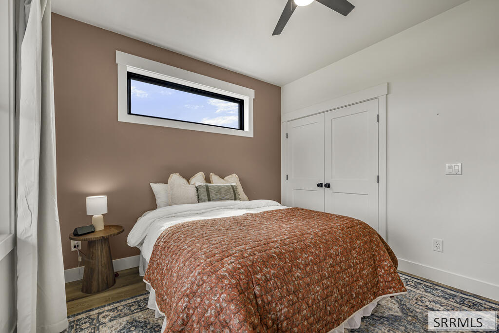 Staged bedroom with a rust-patterned quilt, taupe accent wall, and high horizontal window.