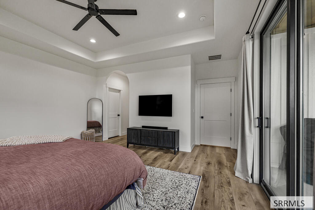 Furnished bedroom with a mauve bedspread, tray ceiling, wall-mounted TV, and sliding glass doors.
