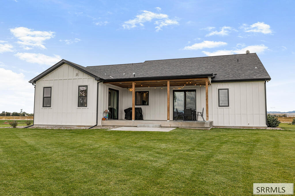 Rear of a white home with a covered patio and outdoor seating overlooking a broad lawn.