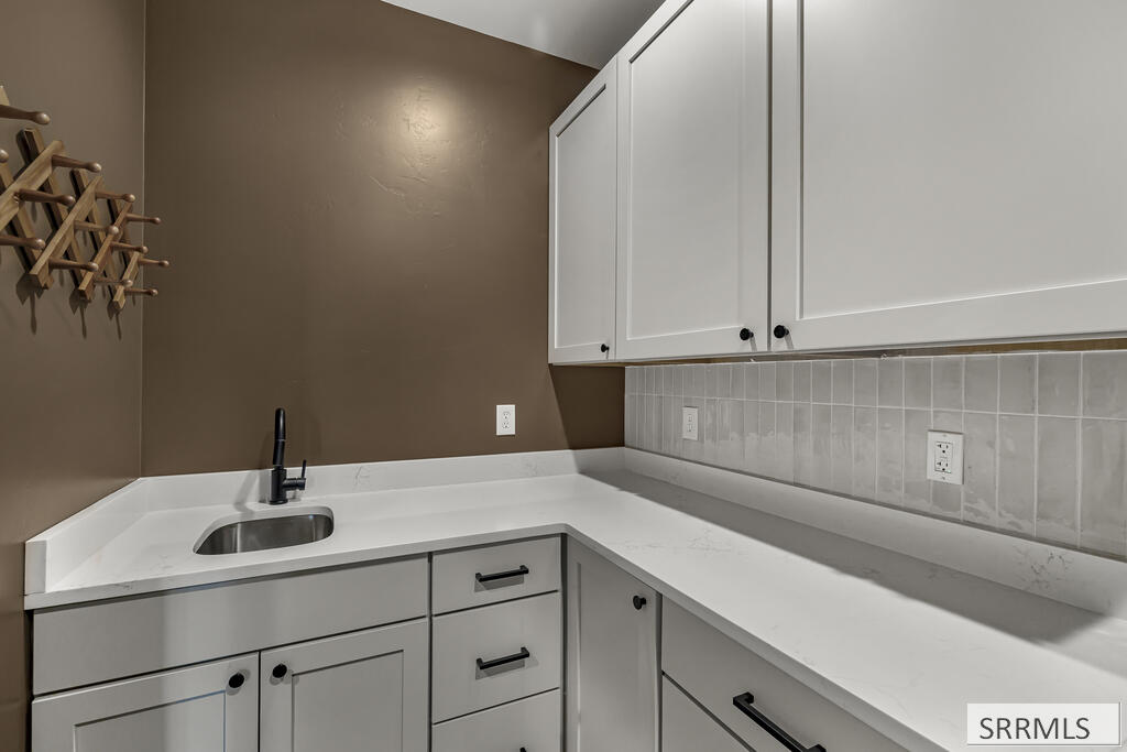 Kitchen counter with a small sink, white cabinets, tiled backsplash, and wooden wine rack.