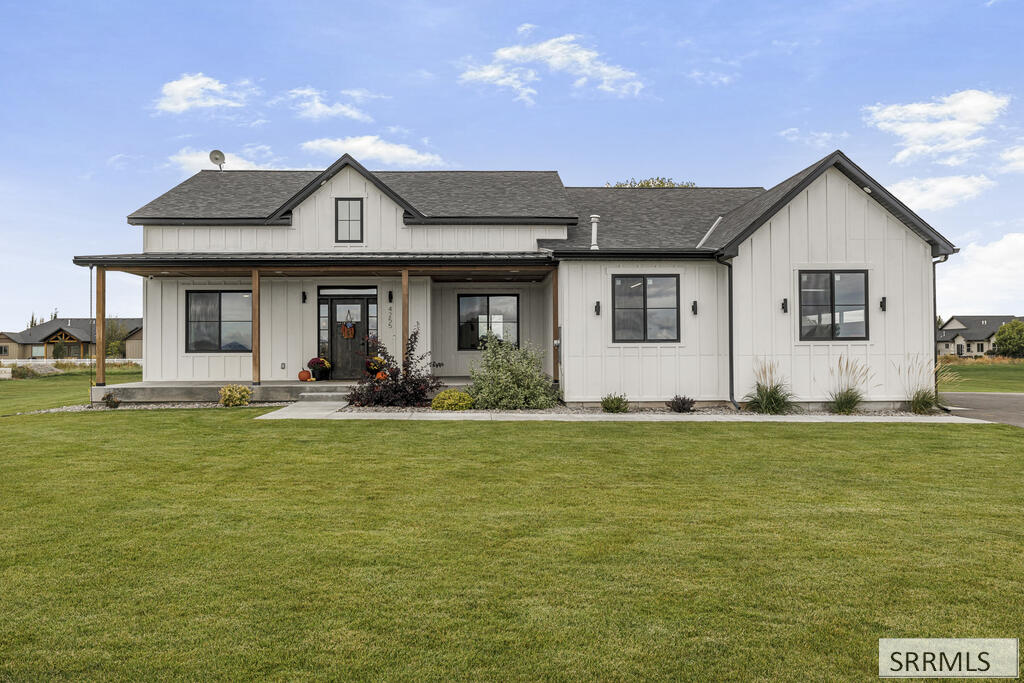 White modern farmhouse with a covered porch, dark gabled roofs, and a broad green lawn.