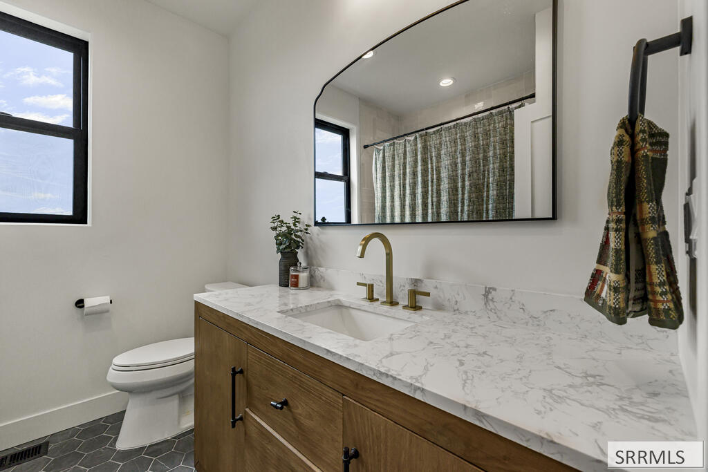 Bathroom with a wood vanity, marble counter, brass faucet, and toilet beside a window.