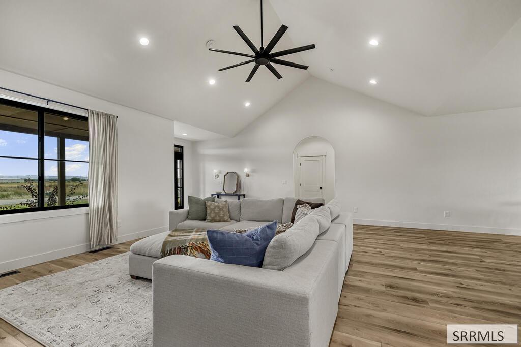 Staged living room with vaulted ceiling, large windows, sectional sofa, and wood-look flooring.