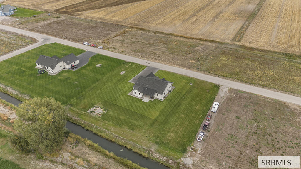 Aerial view of two homes on large green lots beside a canal and rural fields.