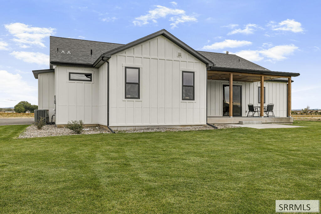 Rear exterior of a white home with a covered patio and broad green lawn.