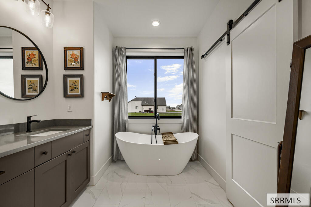 Bathroom with a freestanding tub beneath a large window and a gray vanity.