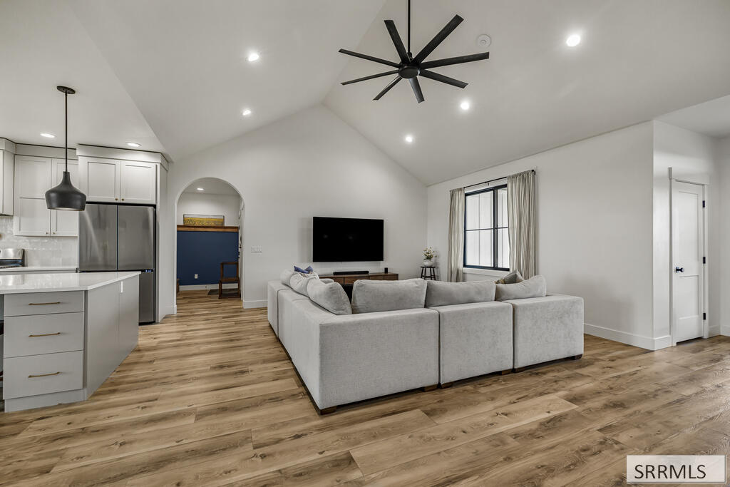 Open-plan living room with vaulted ceiling, gray sectional, wall-mounted television, and adjoining white kitchen.