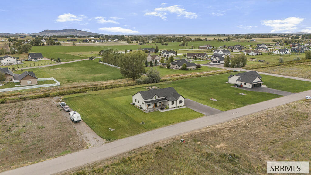 Aerial view of a home on a large lot amid a Rexburg neighborhood, fields, and distant hills.