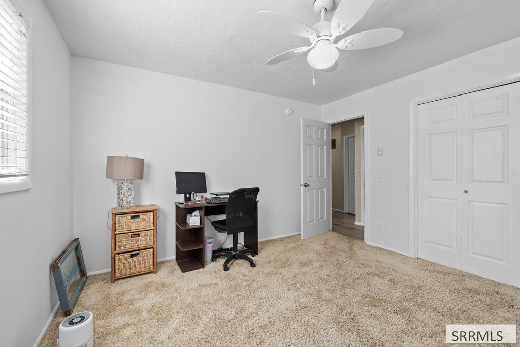 Carpeted bedroom with a desk, wicker drawers, ceiling fan, and double closet doors.