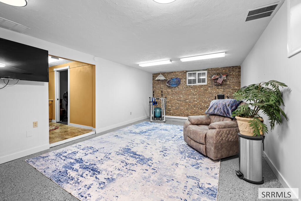 Basement recreation room with a blue-and-white rug, recliner, exercise equipment, and brick accent wall.