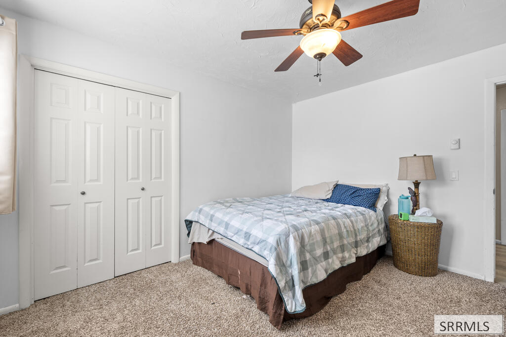 Bedroom with a plaid-covered bed, double closet doors, and a ceiling fan.