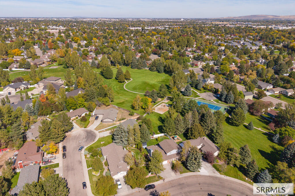 Aerial view of a leafy neighborhood surrounding a green park and blue tennis courts.