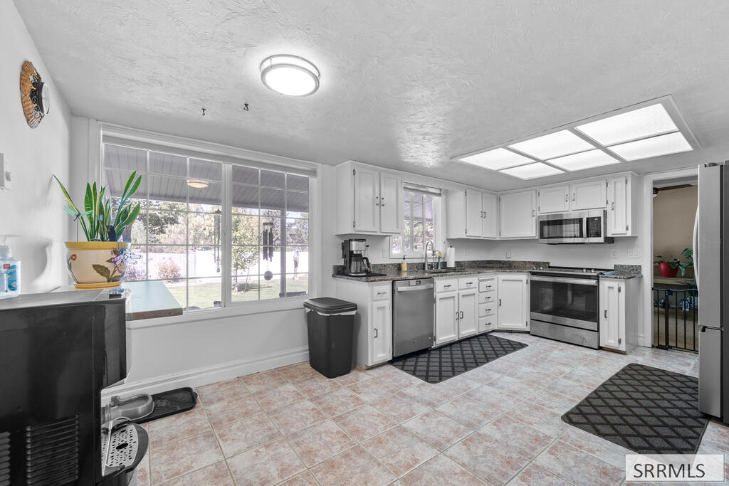 Kitchen with white cabinets, stainless appliances, patterned tile floor, and large windows overlooking a snowy yard.