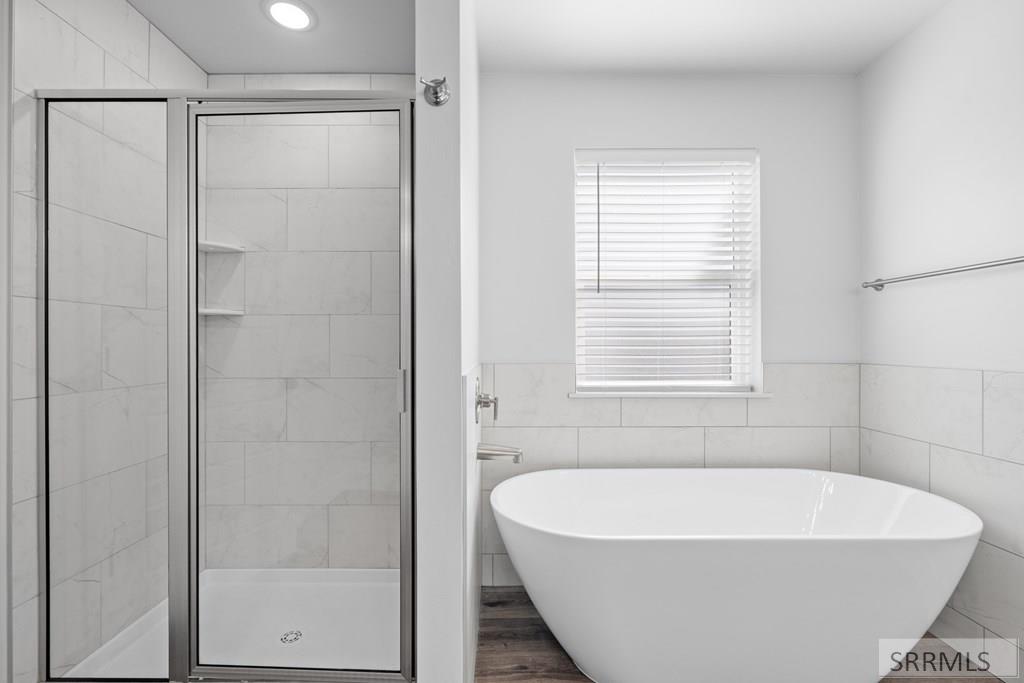 Bathroom with a glass shower, freestanding tub, tiled walls, and a window with blinds.