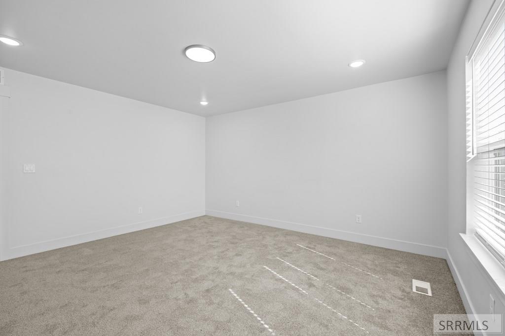 Empty carpeted room with white walls, recessed lights, and a window with blinds.